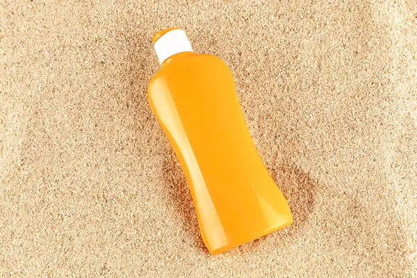 Turuncu güneş kremi şişesi kum arka planında izole edilmiş. Yüksek kalite fotoğraf