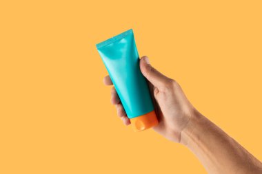 El ele tutuşan güneş kremi turuncu arka planda izole edilmiş. Yüksek kalite fotoğraf