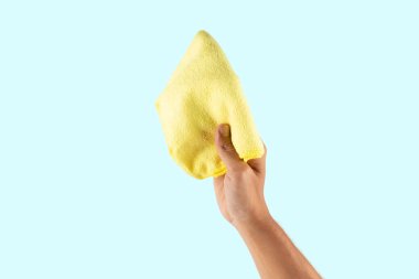 Cyan arka planda izole edilmiş sarı bir temizlik bezini tutan erkek el. Yüksek kalite fotoğraf