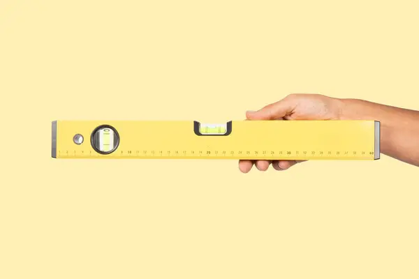 Sarı arka planda izole edilmiş sarı su ölçer tutan bir erkek el. Yüksek kalite fotoğraf