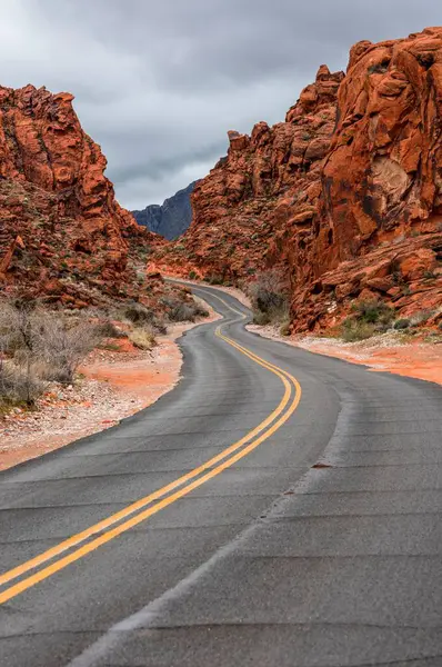 沙漠中的孤寂 孤独驾驶在漆黑的黑色道路 红色岩石和雄伟的山脉上 — 图库照片