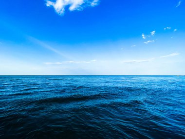 Mavi gökyüzü, bulutlar ve rüzgar dalgalarıyla sakin okyanus ufku.