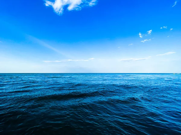 Tranquil ocean horizon with blue sky, clouds, and wind waves.