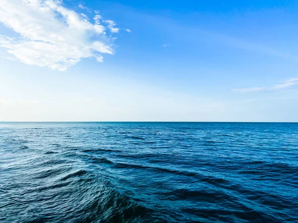 Tranquil ocean horizon with idyllic blue sky and rolling waves.