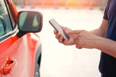 Telefonu açık havada arabasının yanında duran bir adamın elinde. Modern yaşam tarzı