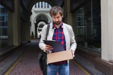 Genç bir erkek ofis çalışanı, bir şehir sokağının arka planına karşı işten çıkarma ile ilgili bir belge okuyor. Yaş, iş, serbest çalışma, yaşam tarzı konsepti