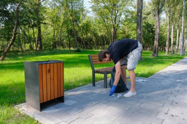 Genç adam dışarıda, parkta çöp topluyor. Ekoloji kavramı, çevre kirliliği sorunları