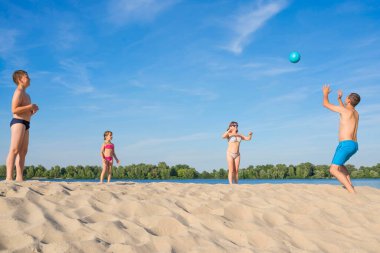 Mutlu bir aile güneşli bir günde nehir kenarında voleybol oynuyor. Yaşam tarzı. Yaz tatili.
