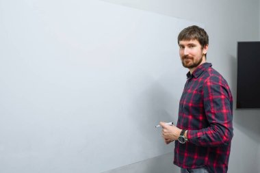 Ofiste çalışan genç bir adam, beyaz bir duvara karşı duruyor ve fotokopi çekilen kameralara bakıyor..