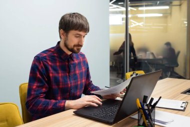 Ofis masasında oturan bir iş adamı dizüstü bilgisayarla çalışıyor. Ofisteki masasında oturan genç bir adamın portresi..