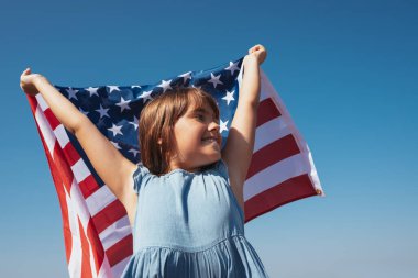 Gökyüzünün arka planında elinde Amerikan bayrağı olan mutlu bir kızın portresi..