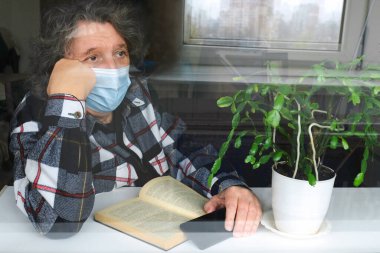 Karantinada koruyucu maskeli yaşlı bir adam pencereden bakıyor. Kendini izole etme, salgın hastalık, yaşam tarzı. Sağlık hizmeti kavramı.