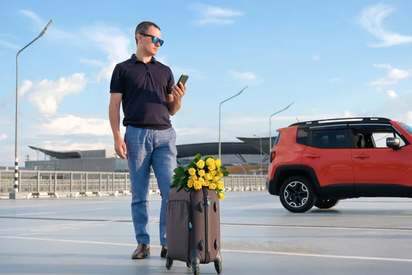Otoparkta Bavulları Çiçekleri Olan Genç Bir Işadamı Taksiyi Telefonla Arıyor — Stok fotoğraf