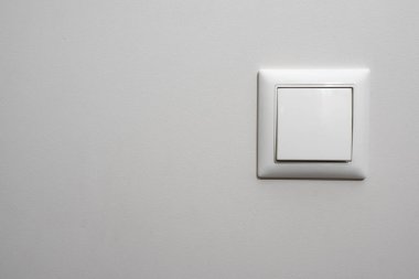 Beyaz ışık anahtarı, açık gri bir duvara yerleştirilmiş beyaz rengin plastik mekanik anahtarı..
