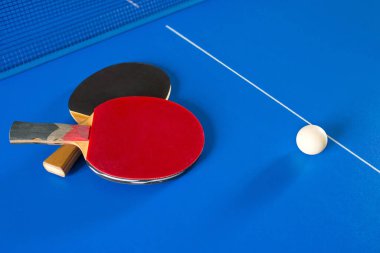 Masa tenisi için iki raket ve mavi masada beyaz bir top. Masa tenisi oyunu. Spor oyunları.