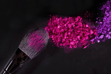 Siyah arkaplanda makyaj fırçaları ve renkli göz farı, üst görünüm.