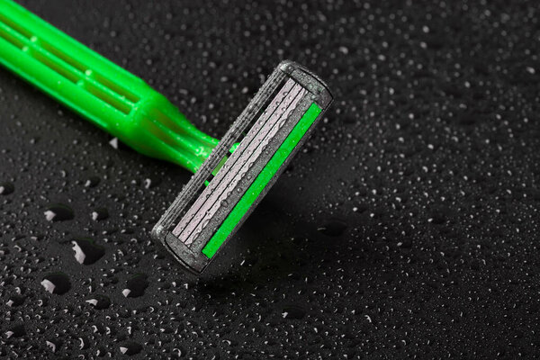 New razor blade with drops of water on a black background. Close-up.