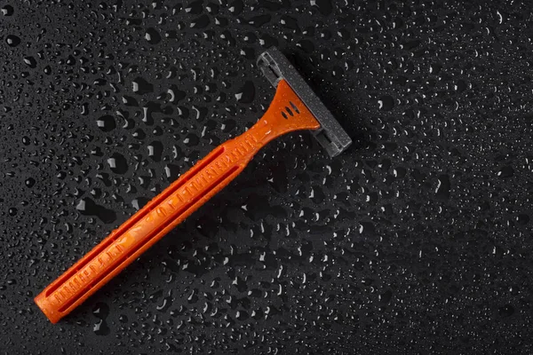 Disposable razor with drops of water on a black background. Skin care concept.