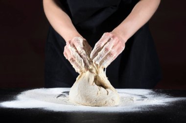 Dişi eller hamuru siyah ahşap bir masada yoğurur. Yiyecek konsepti.