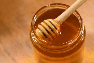 Ahşap kepçe, ballı ve cam kavanozlu, yakın plan bir masa üzerinde. Organik arıcılık ürünleri.