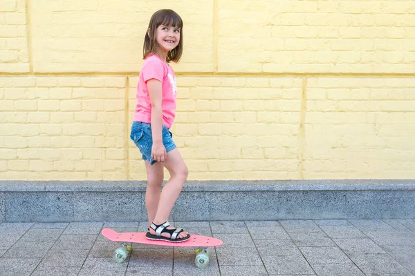 幸せな子供は 黄色いレンガの壁の背景に都市のスケートボードに従事しています スポーツの生き方 — ストック写真