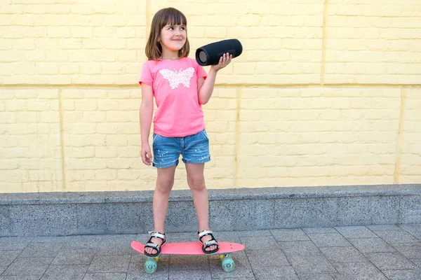 かわいい女の子は音楽を聴き レンガの黄色い壁の背景に対してスケートボードに乗ります スポーツ ライフスタイル — ストック写真