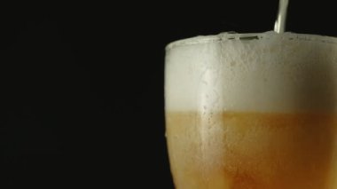 Köpüklü bir bardak light bira yavaşça siyah arka planda döner. Soğuk bira bardağa dökülür. Yakın plan..