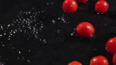 Siyah bir masanın ıslak yüzeyine düşen olgun domatesler, su damlaları. Hasat.