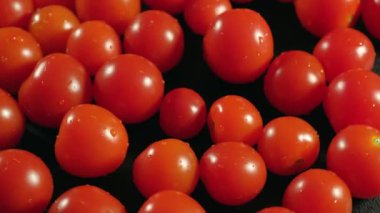 Olgun kırmızı domatesler ve su damlaları siyah bir masada dönüyorlar. Yemek konsepti, yemek. Hasat.