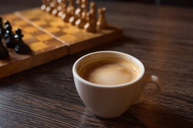 Tahta bir masada bir fincan kahve ve satranç tahtası..