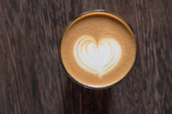 Picture in form a heart, in the cup of coffee on a wooden background. Kind from above.