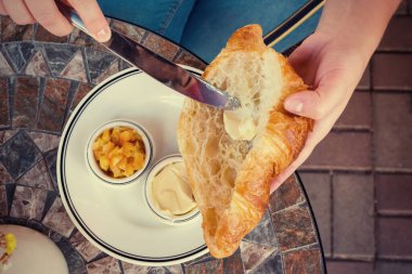 Dişi eller taze kruvasana yağ sürer. Üst görünüm.