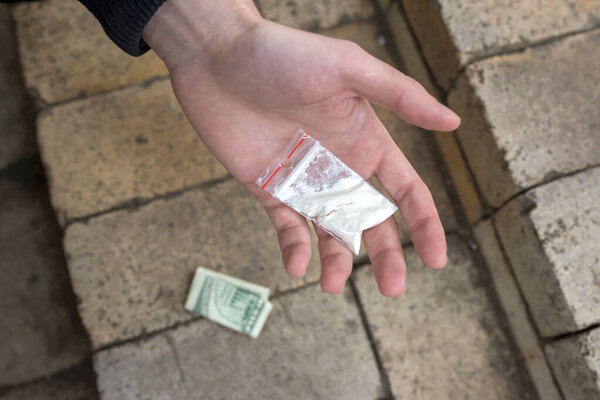 Hand of an addict holding a plastic bag in his palm with cocaine powder or other drugs. Close-up. Addiction concept.