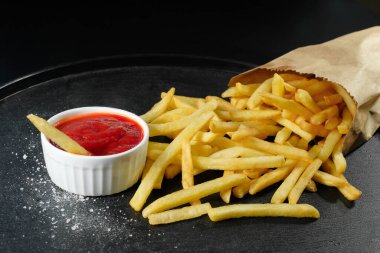 Koyu arkaplanda bir parça patates ve ketçap. Fast food, yakın çekim..