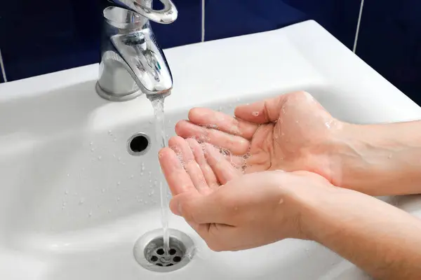 Hands under the tap with water over the sink in the bathroom. Hygiene concept.