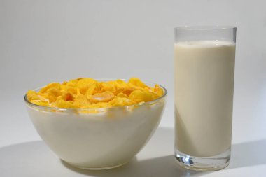 Gri arka planda bir kase mısır gevreği ve bir bardak süt..