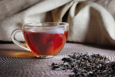 Koyu arkaplanda bir bardak çay ve yapraklar. Yakın plan..