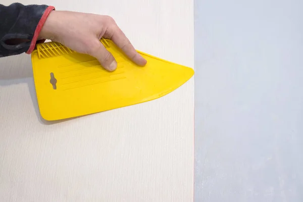 stock image A worker smoothes wallpaper with a plastic yellow spatula.