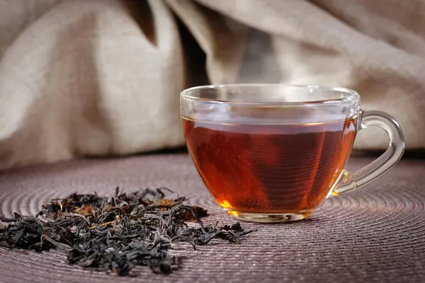 A cup of black tea and leaves on a dark background.