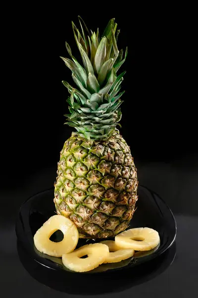 Pineapple and pineapple slices on a black plate, on a dark background.