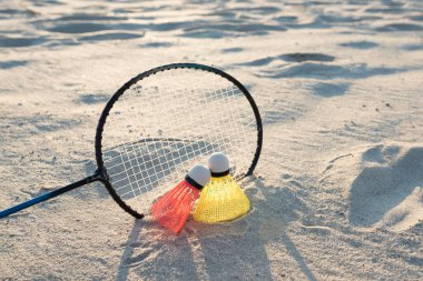 Spor oyunları ve yaz tatili konsepti. Plaj badmintonu. Gün batımında raket ve iki mekik horozu kumsalda..