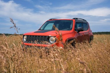 Bir tarlada sarı çimlerde duran turuncu SUV. Keşif gezisi ya da aşırı off-road gezisi. Ulaşım, seyahat kavramı.