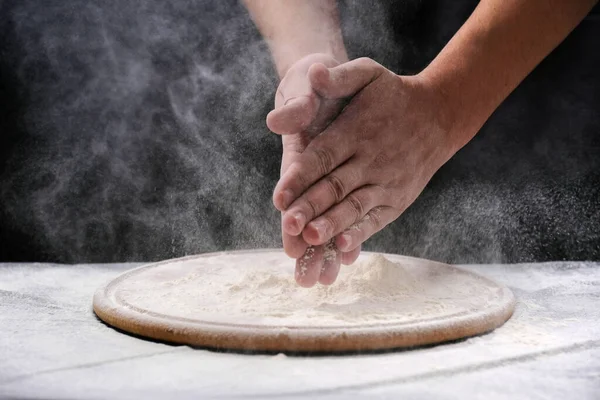 A man claps his hands with a splash of white flour and a black background. Preparing Meal, Hands in flour.