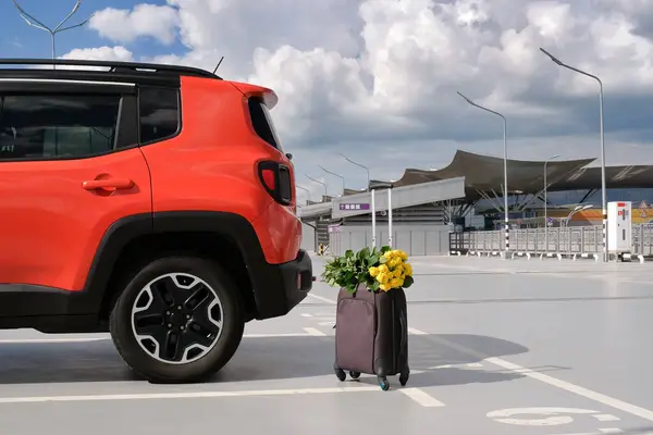 全家人的橙色车 行李箱和一束鲜花在一个空荡荡的机场停车场 暑假的概念 — 图库照片