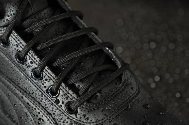 Siyah arka planda su damlaları olan yeni su geçirmez deri botlar. Ayakkabı konsepti. Kış ayakkabıları.
