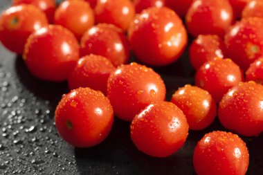 Siyah mutfak masasına su damlatan kırmızı domatesler. Taze sebze..