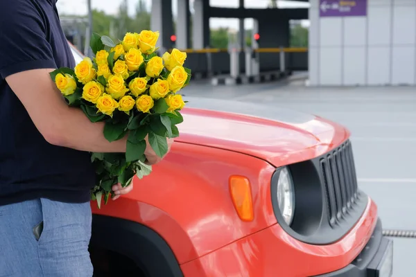 一个男人拿着一束黄色的玫瑰和一辆汽车在停车场的剪影 旅行概念 — 图库照片