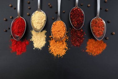 Siyah arka planda baharatlı kaşıklar. Yukarıdan bak. Kaşıktaki renkli baharatlar.