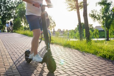 Güneşli bir günde modern bir scooterla parkta genç bir adam. Ekolojik Taşıma.