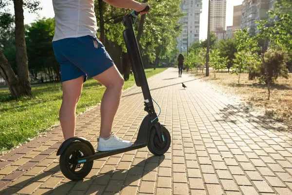 Güneşli bir günde, şehir caddesinde, modern bir scooter kullanan bir adam. Şehir yaşam tarzı. Çevre dostu ulaşım.